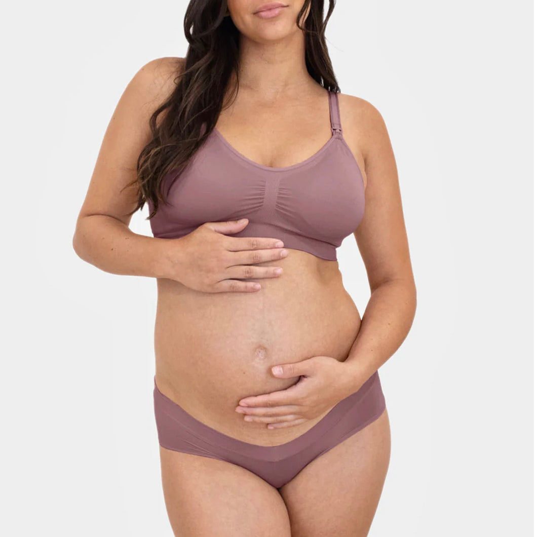 Pregnant woman wearing a matching bra and underwear set in a soft purple color on a white background.